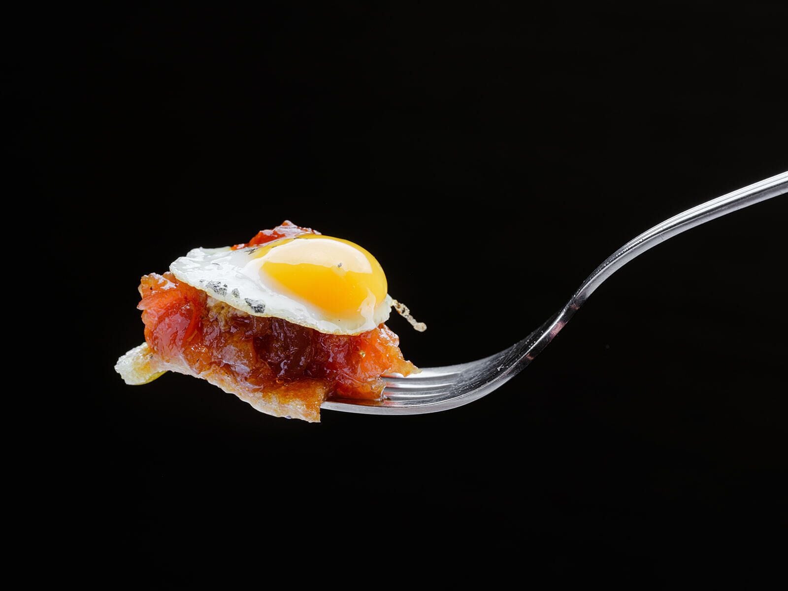 A fork with a piece of food that appears to be a fried egg on top of a slice of meat.