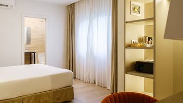 Une chambre d’hôtel comprenant un lit, un bureau, une chaise, une étagère avec quelques objets et une fenêtre avec des rideaux.