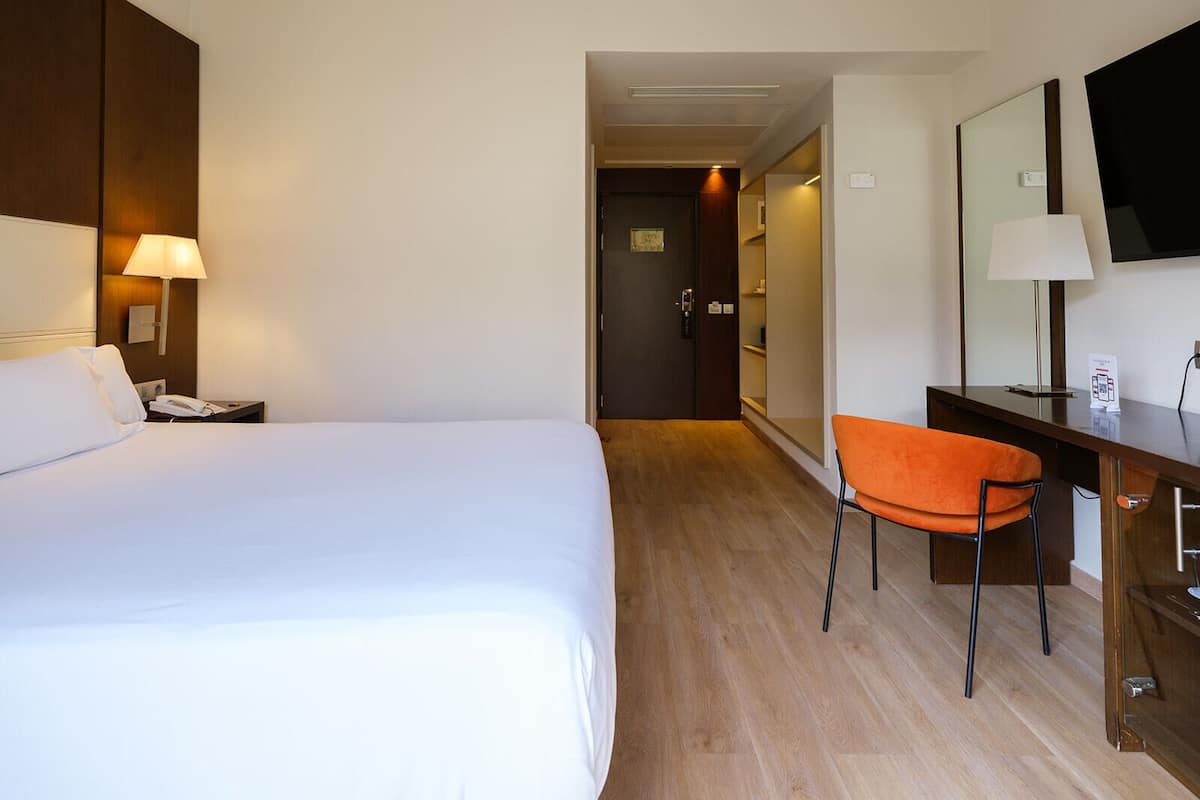 Una habitación de hotel con cama, escritorio y silla, televisor y una puerta que da a otra habitación.
