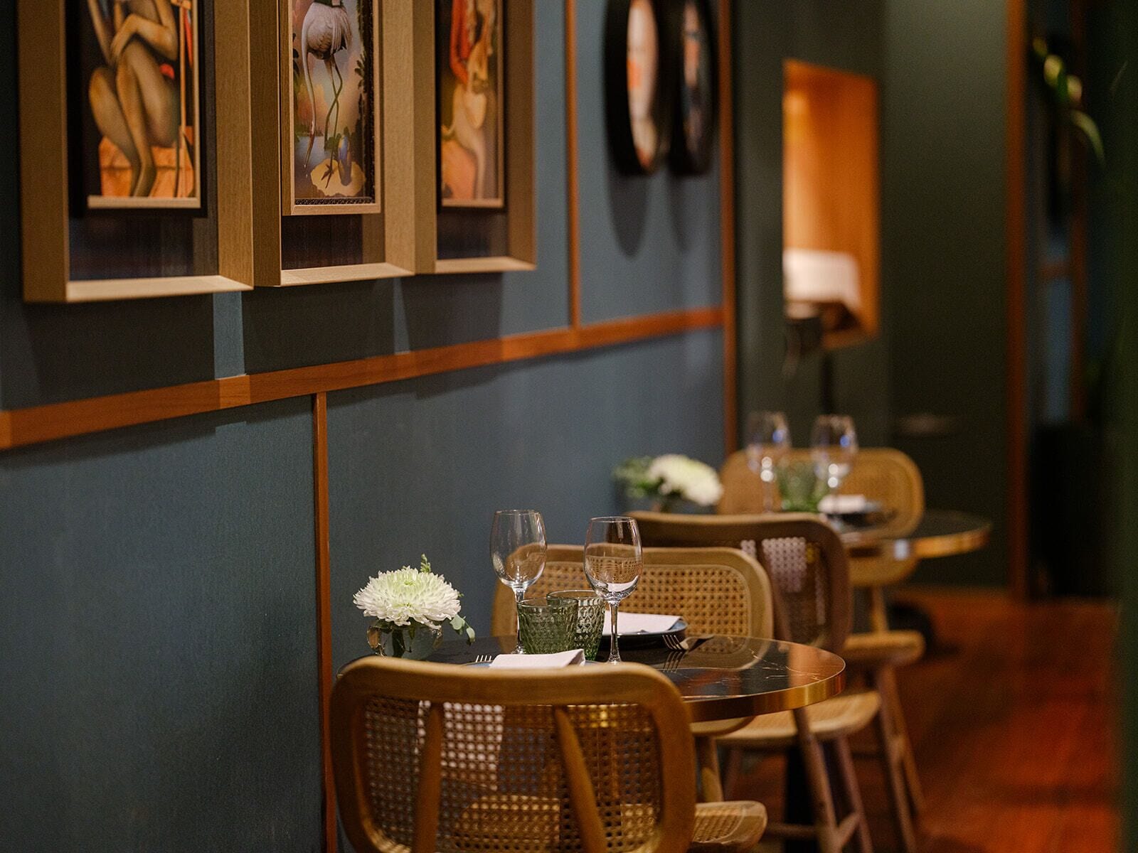 Un restaurant avec une rangée de tables et de chaises, chacune agrémentée d’un verre et d’un arrangement floral.