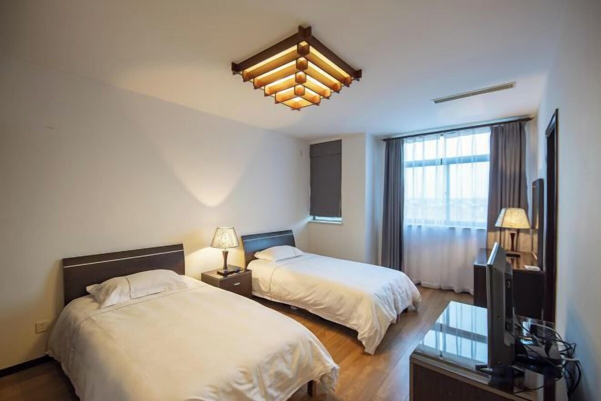 A hotel room with two beds, a TV, a lamp, and a window with curtains.