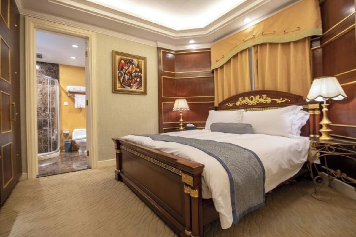 A hotel room with a large bed, a shower area, and a painting on the wall.