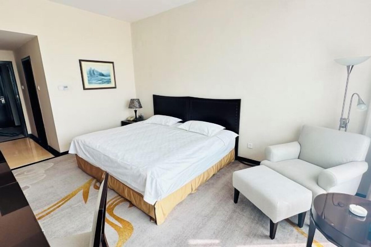 A hotel room with a bed, a chair, a desk, and a lamp.