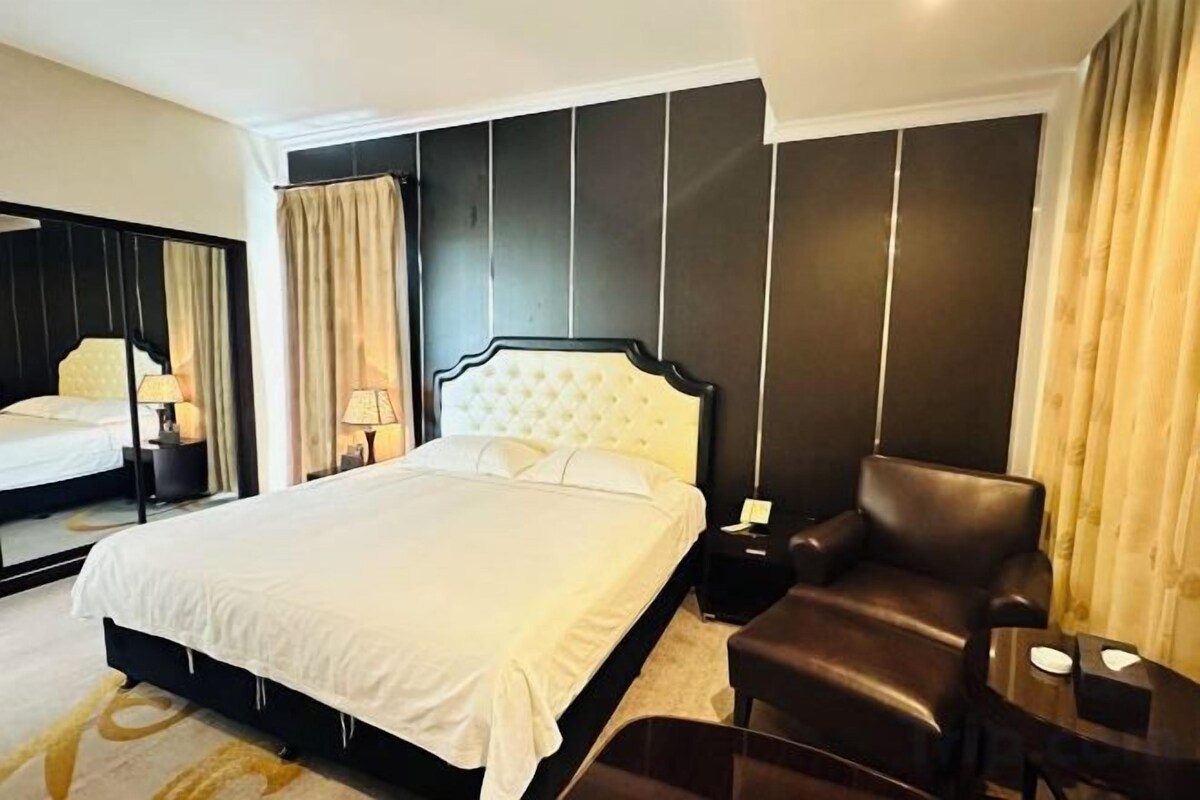 A hotel room with a large bed, a leather armchair, a bedside table, and a mirror.