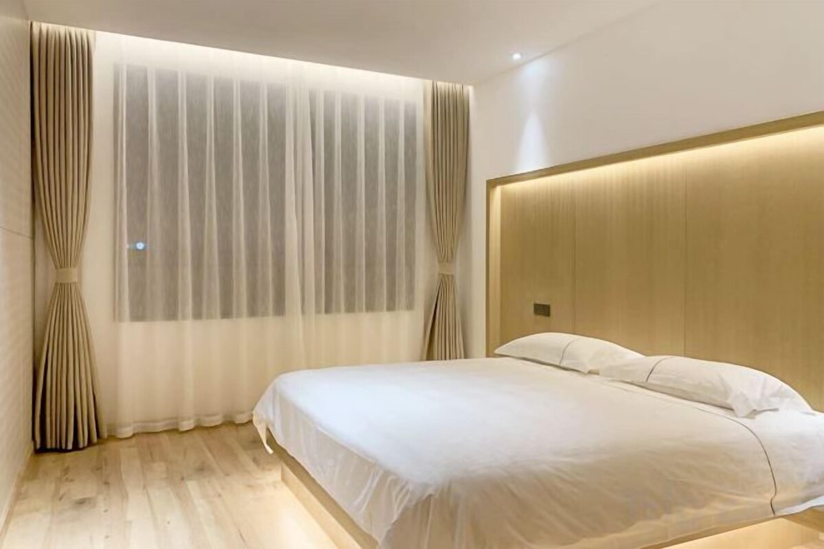 A hotel room with a large bed, a wooden headboard, and sheer curtains.