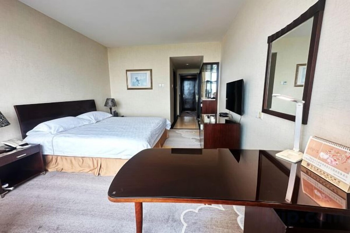 A hotel room with a bed, bedside table, desk, chair, and a mirror.