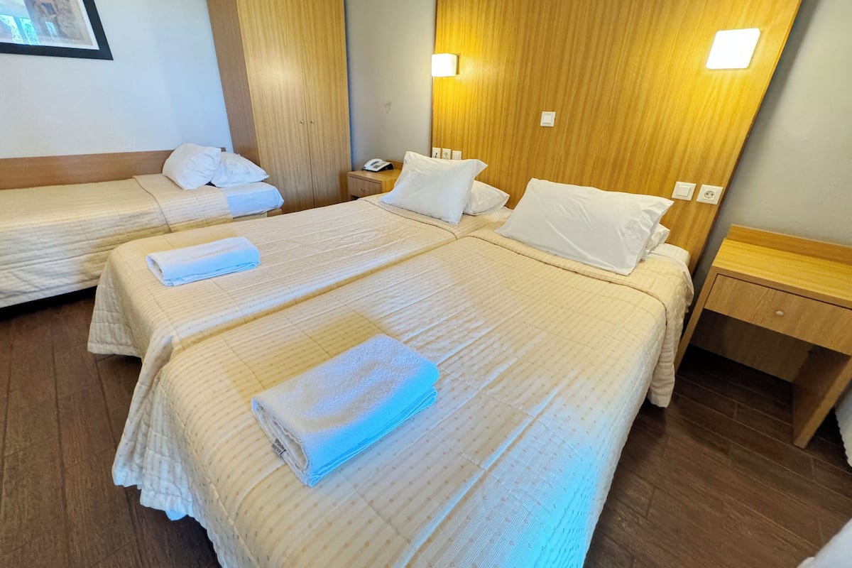 A hotel room with two beds, each with a neatly folded towel, wooden headboard, bedside tables, and a framed picture on the wall.