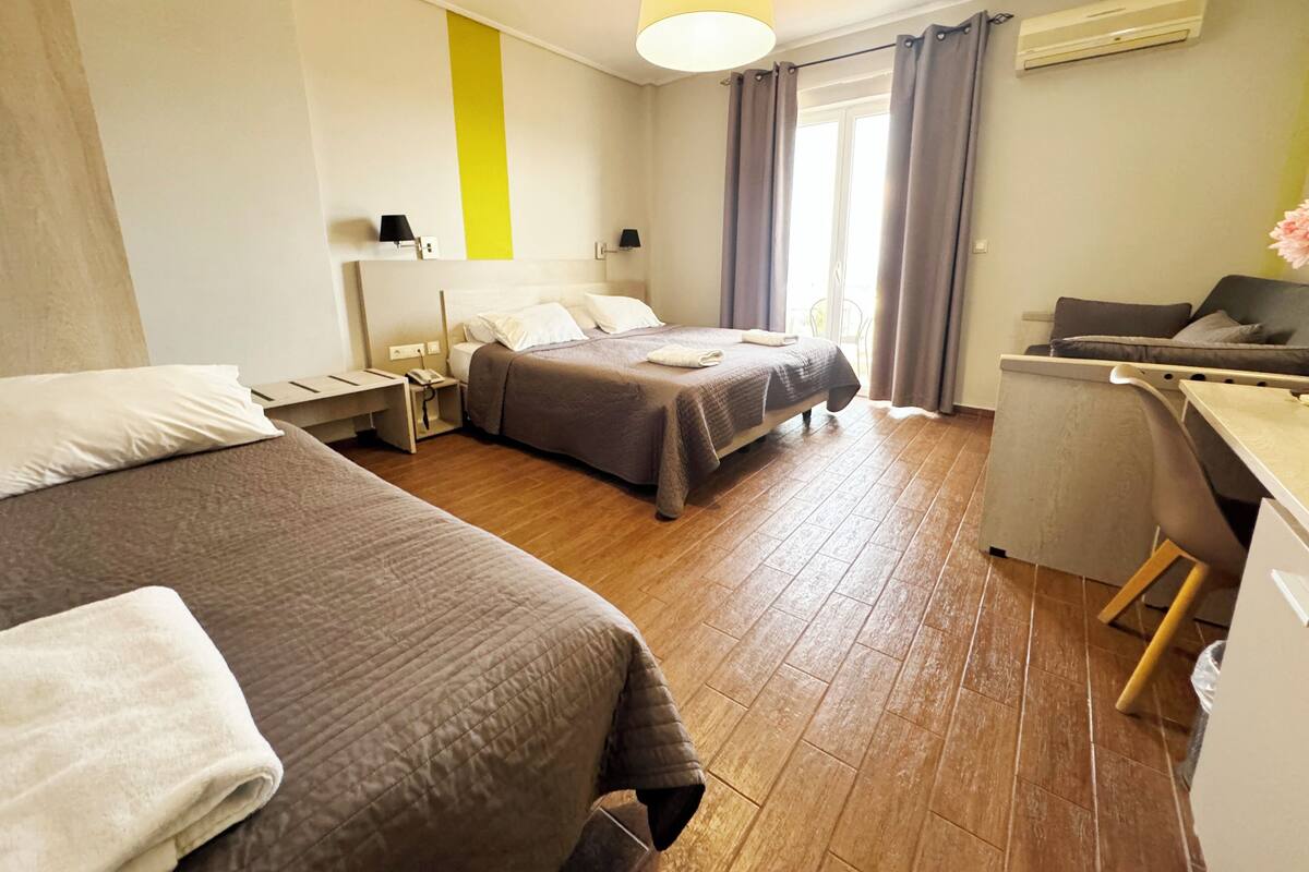 A hotel room with two beds, a desk, a chair, a lamp, and an air conditioning unit.