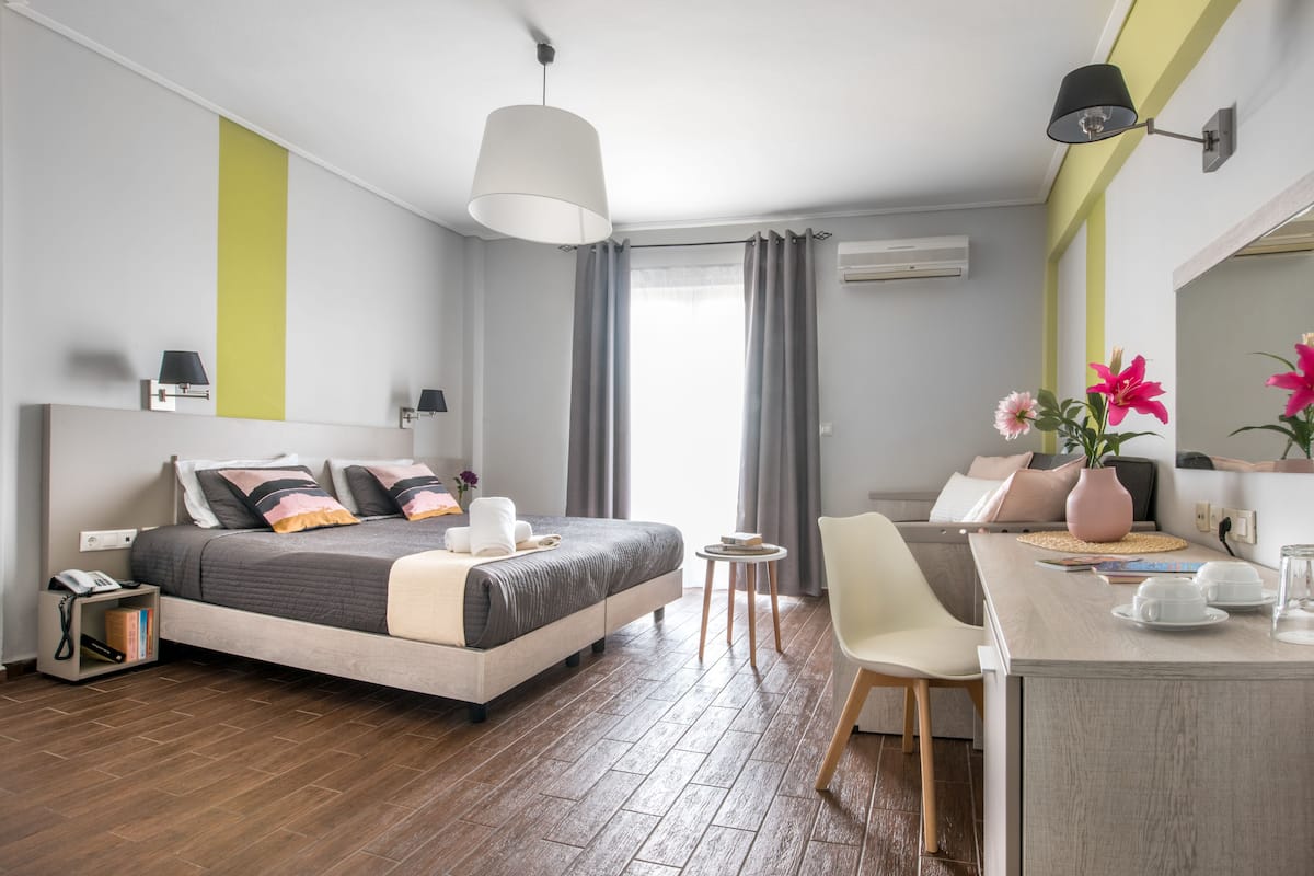 A modern hotel room with a bed, bedside table, chair, and a desk with a lamp.