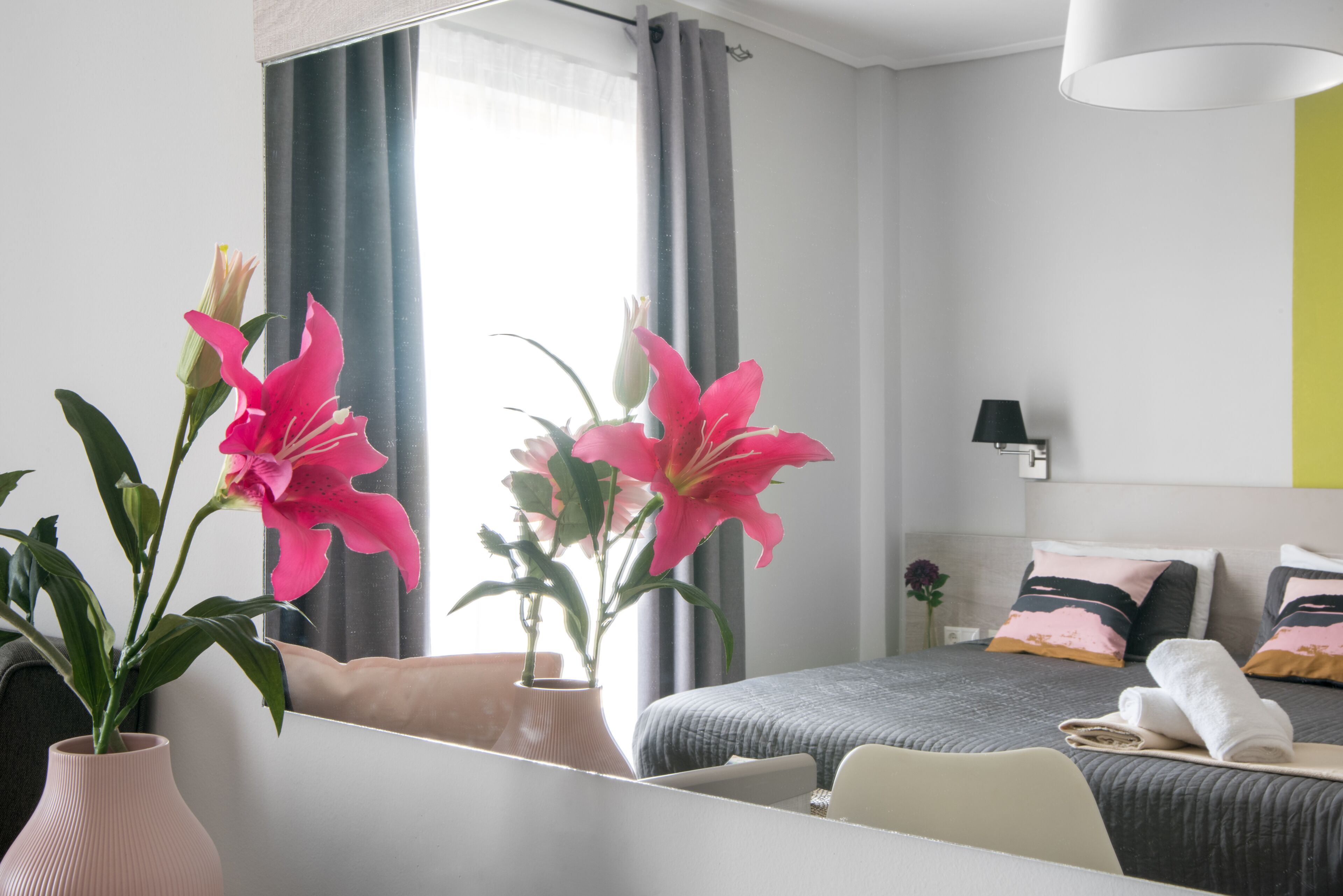 Una habitación de hotel moderna con cama, mesita de noche y un ventanal con cortinas.