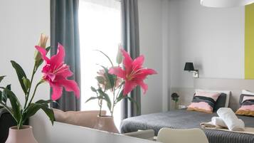 Una habitación de hotel moderna con cama, mesita de noche y un ventanal con cortinas.