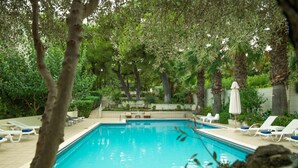 A rectangular swimming pool with clear blue water, surrounded by lounge chairs and a table with a candle and eggs. - Myrto Hotel (Marathon)