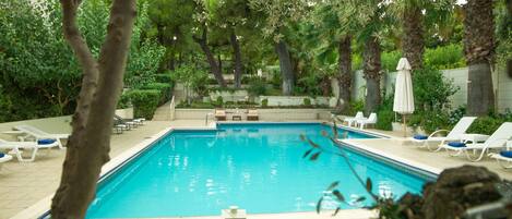 A rectangular swimming pool with clear blue water, surrounded by lounge chairs and a table with a candle and eggs.