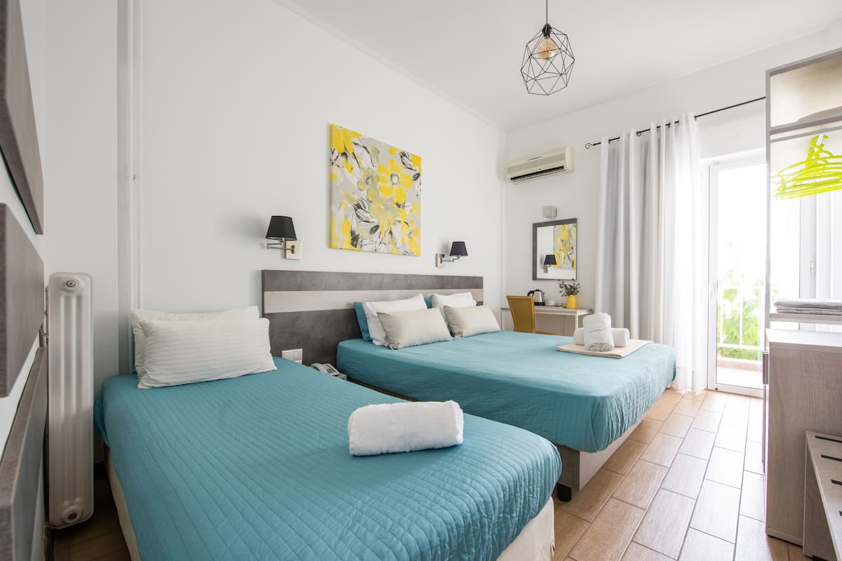 A hotel room with two beds, a large window with curtains, a painting on the wall, and a hanging light fixture.