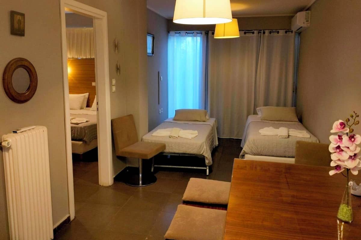 A hotel room with two beds, a sitting area with a chair and a table, a radiator, and a window with curtains.