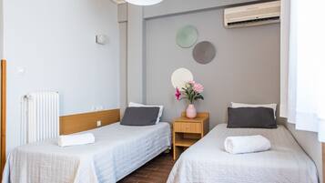 A hotel room with two single beds, a wooden nightstand, a small table, a radiator, and an air conditioning unit on the wall.