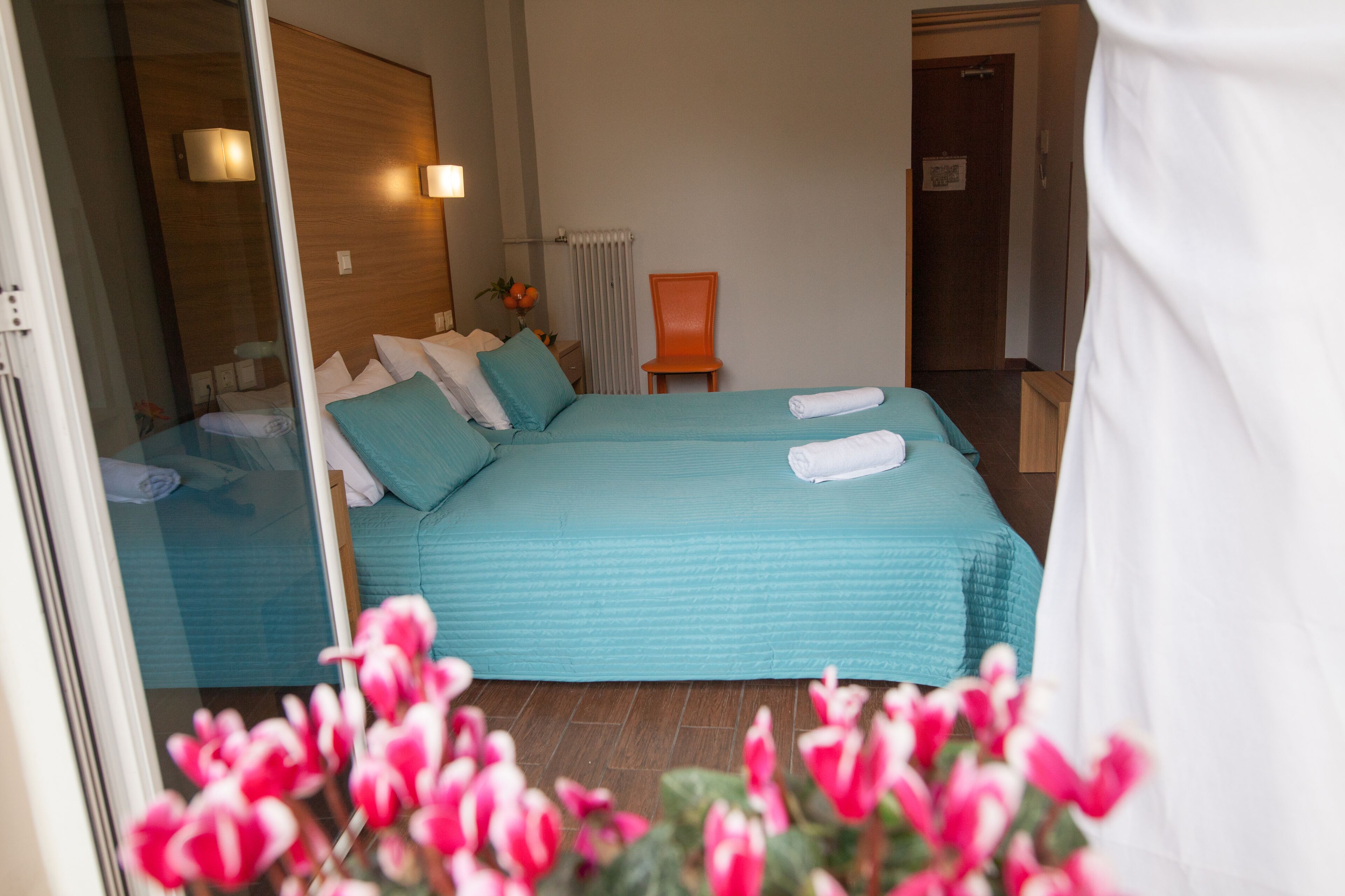 A hotel room with two beds, a chair, a radiator, and a door.