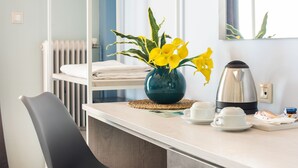 A hotel room with a bed, a bedside table with a vase of yellow flowers, a kettle, and a cup and saucer on the table. - Myrto Hotel (Marathon)