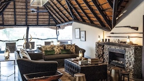 A rustic interior with a high ceiling, a stone fireplace, and a zebra rug. - Jock Safari Lodge (Mbombela)
