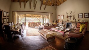 A spacious living room with a dining area, a fireplace, and a large window overlooking a garden. - Jock Safari Lodge (Mbombela)