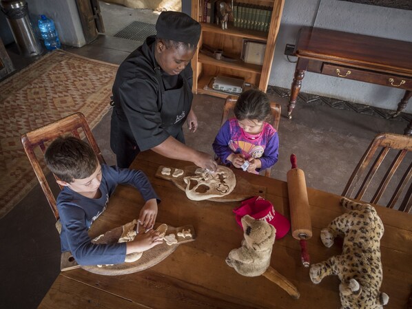A family at a wooden dining table with a leopard plush toy and a rolling pin. - Jock Safari Lodge (Mbombela)