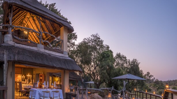 An outdoor dining area with tables and chairs, a pool, and a thatched-roof structure. - Jock Safari Lodge (Mbombela)