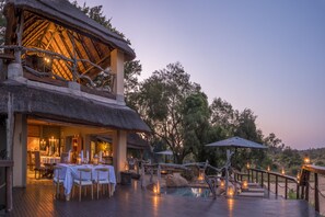 An outdoor dining area with tables and chairs, a pool, and a thatched-roof structure. - Jock Safari Lodge (Mbombela)
