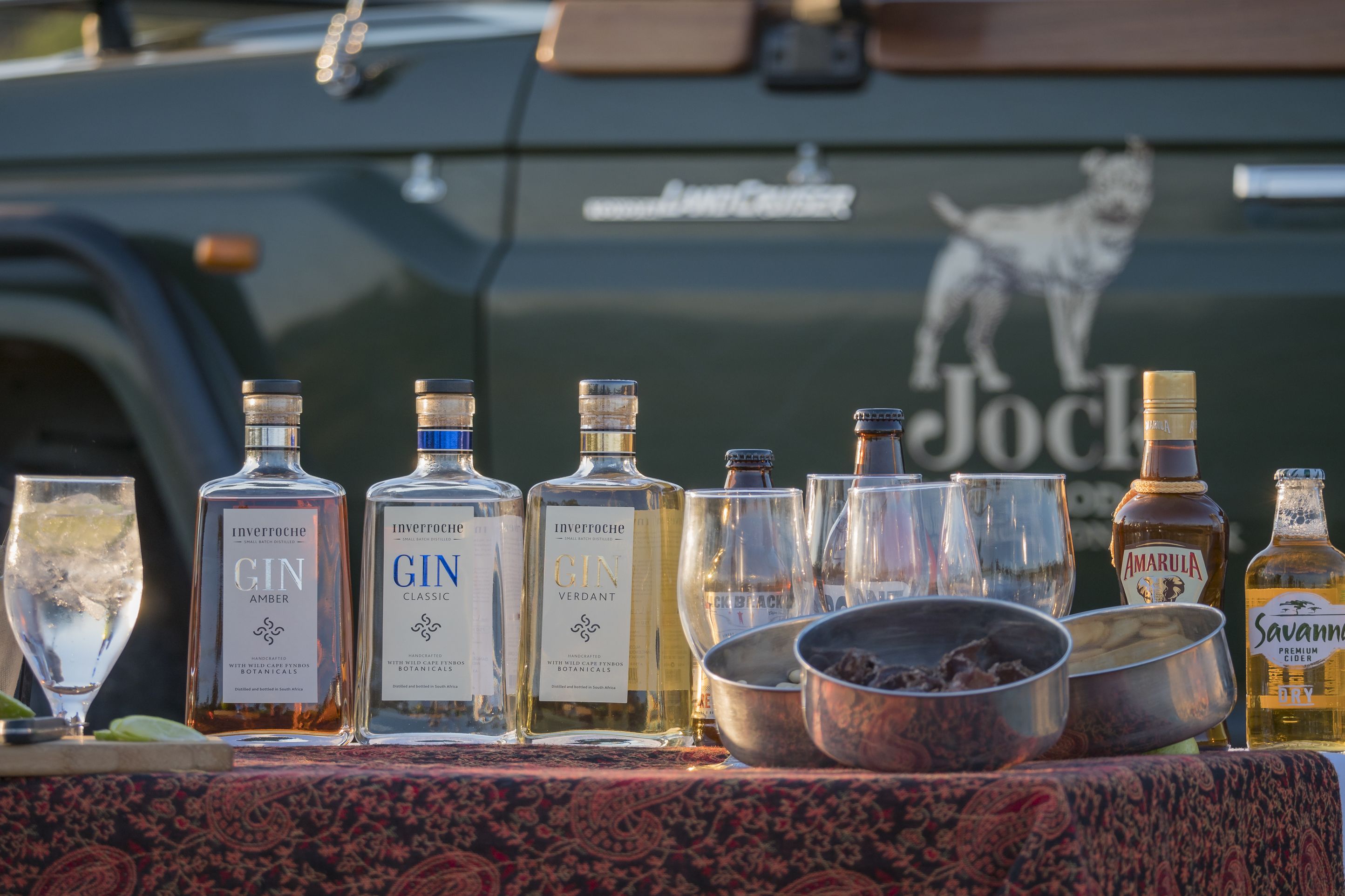 A selection of liquor bottles and glasses on a table in front of a vehicle with a dog decal.