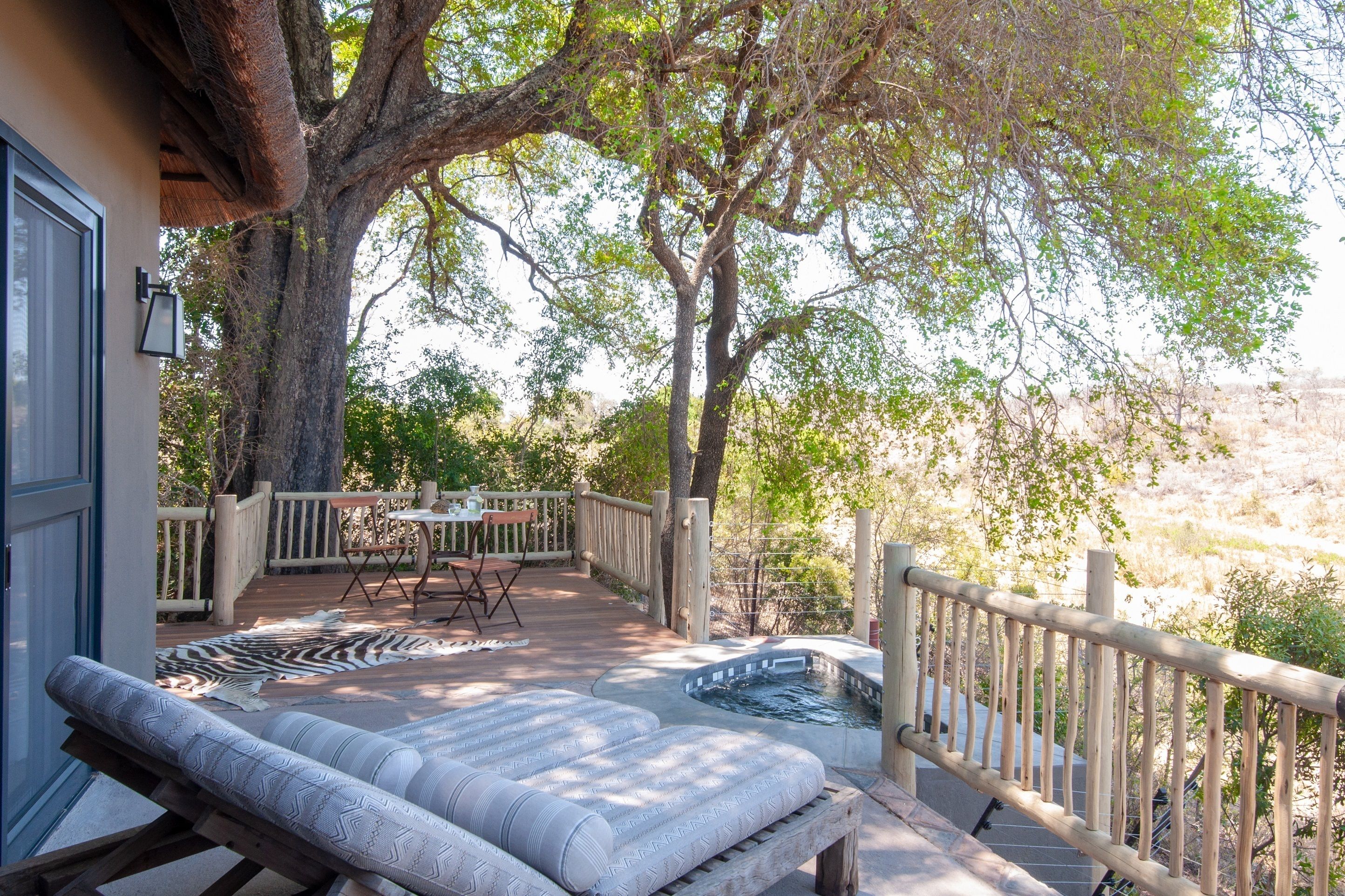 A covered outdoor area with a pool, lounge chairs, and a table with chairs.
