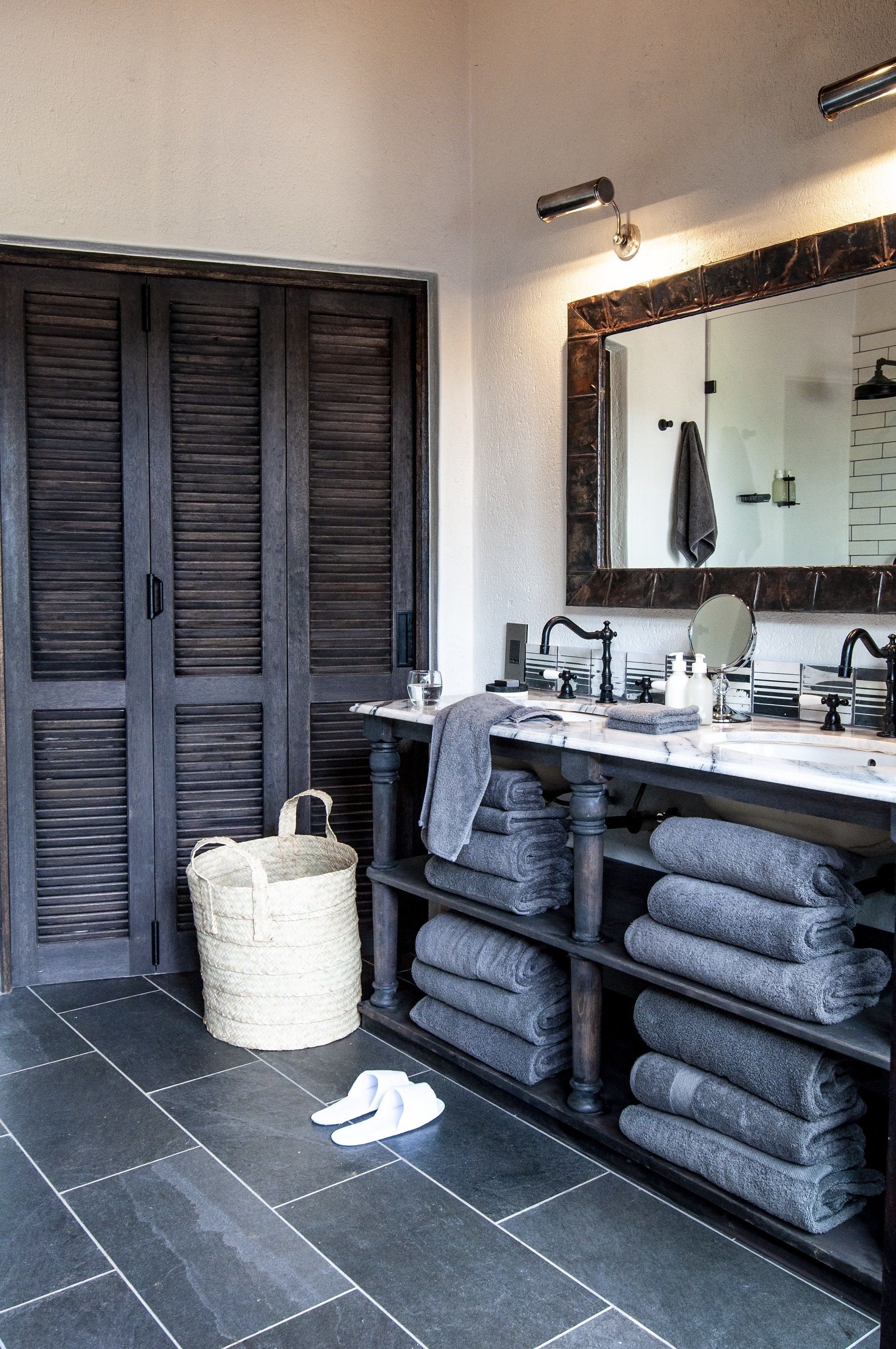 A bathroom with a dark wood door, a marble sink, a mirror, and a towel rack with folded towels.