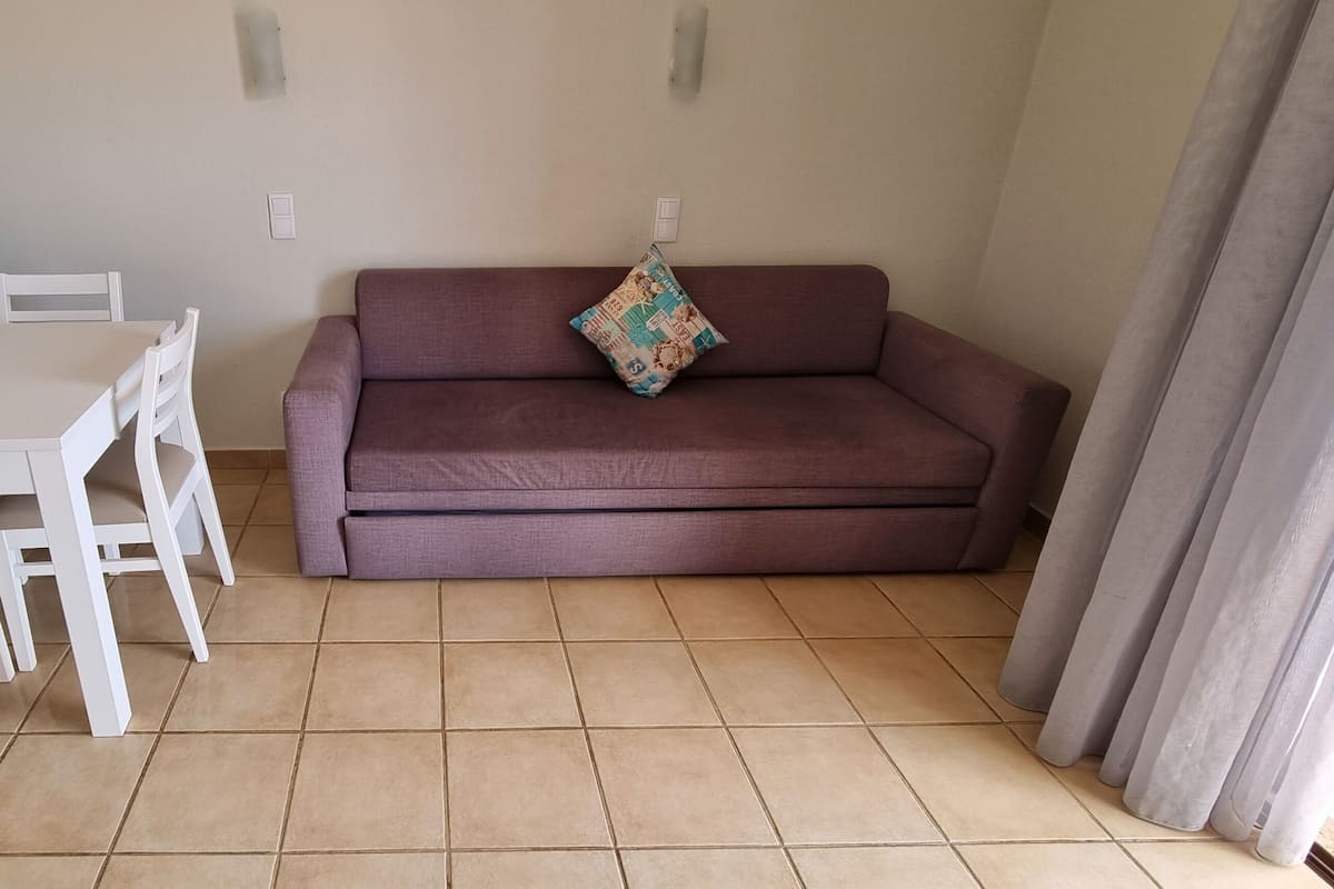 A small living area with a dining table and chairs, a sofa, and a patterned cushion.