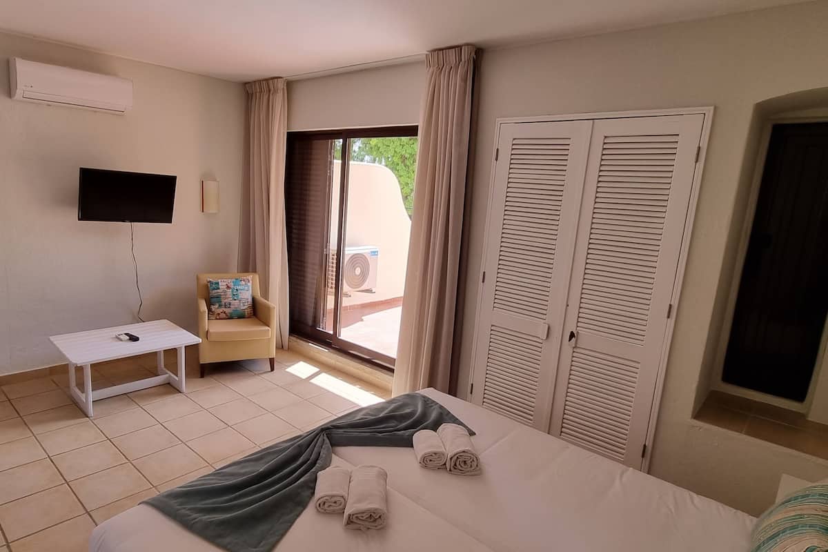 A hotel room with a bed, a desk, a chair, a TV, and a sliding door to the outside.