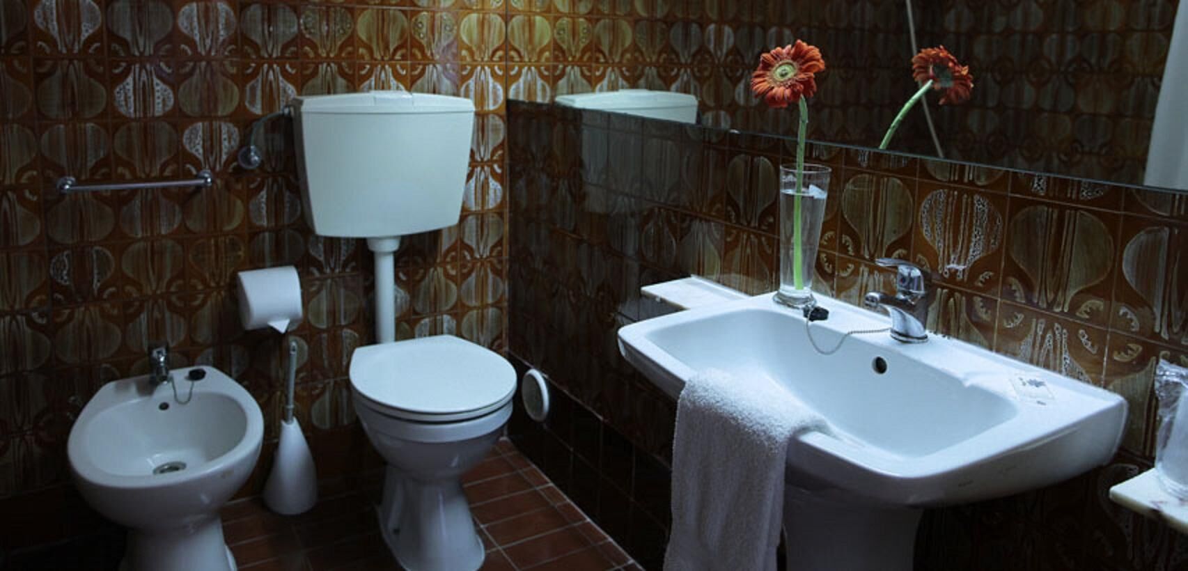 A bathroom with a toilet, bidet, sink, and a towel hanging on the wall.