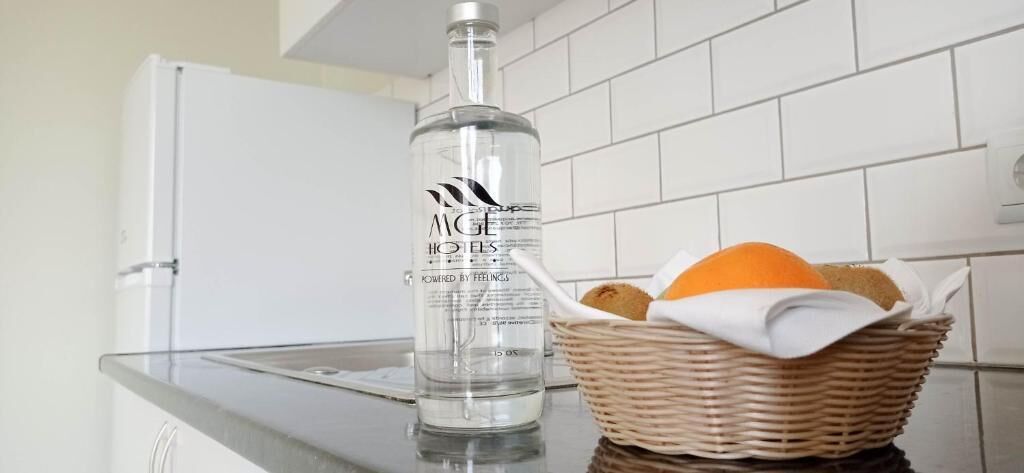 A kitchen counter with a bottle of alcohol, a basket with bread, and a white refrigerator.
