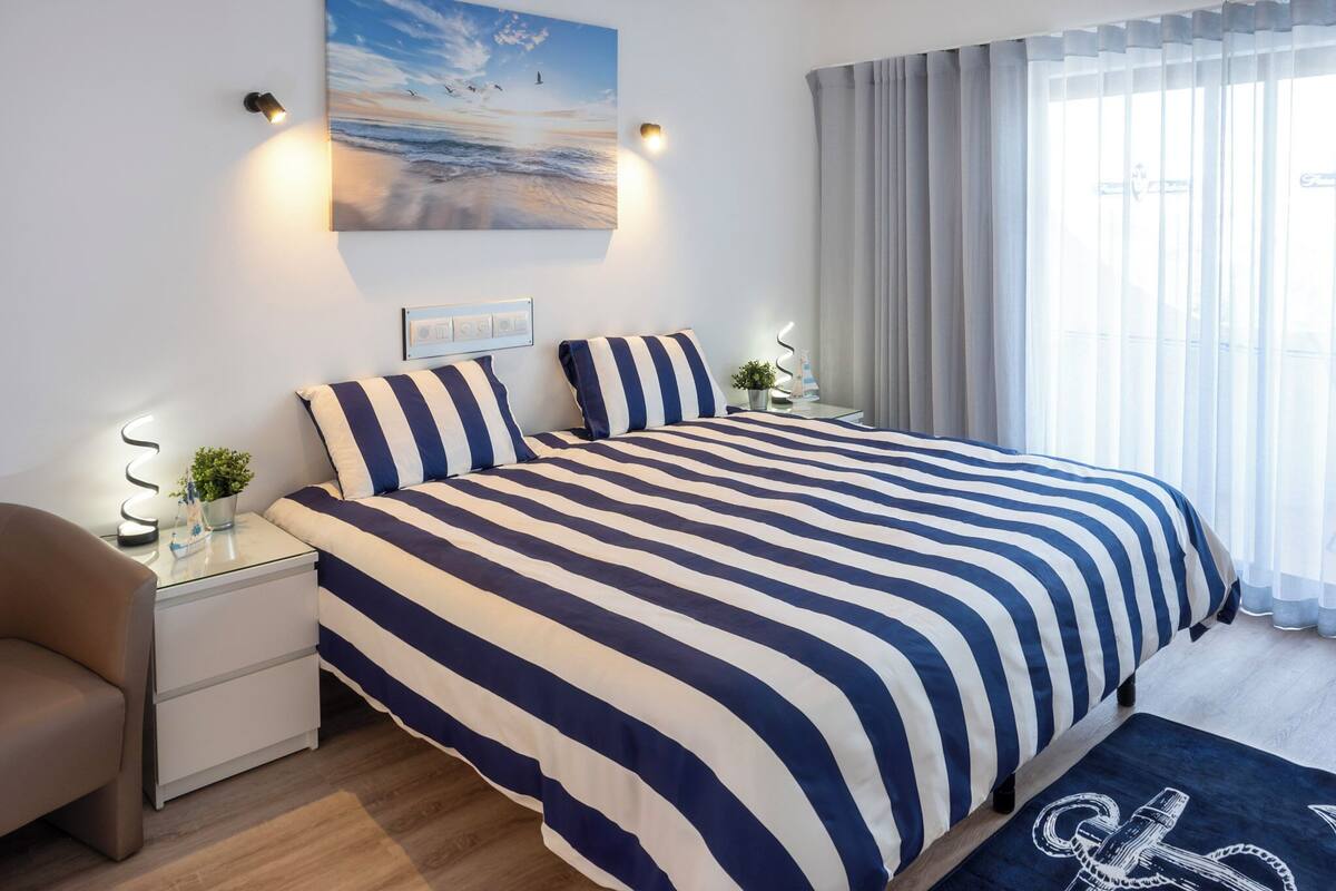 A neatly arranged bedroom with a large bed, bedside tables, a chair, and a painting on the wall.