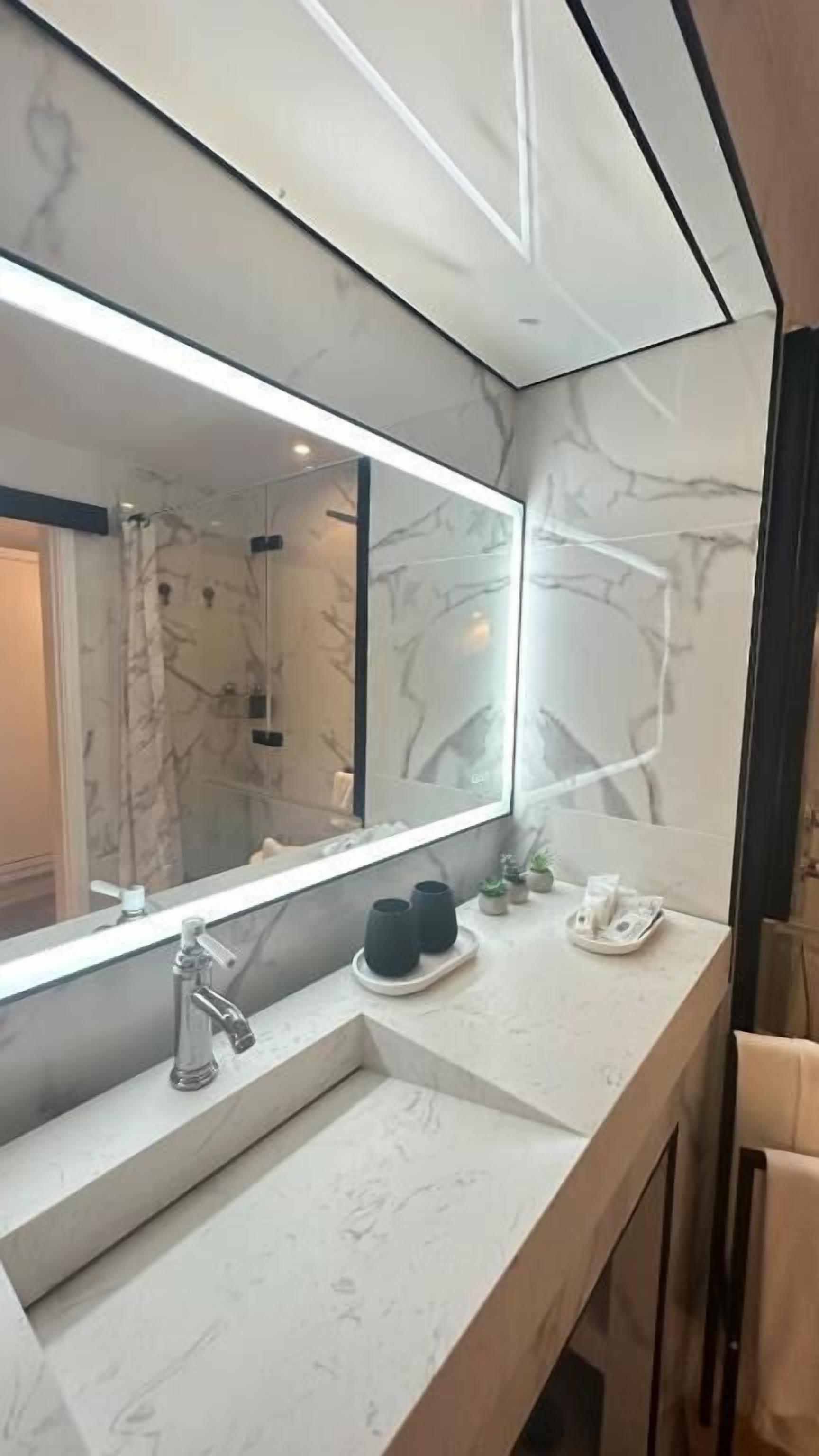 A modern bathroom with a large mirror, a sink, and a shower area.