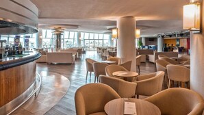 En moderne hotellobby med en buet receptionsdisk, behagelige siddeområder og store vinduer med udsigt over byen.