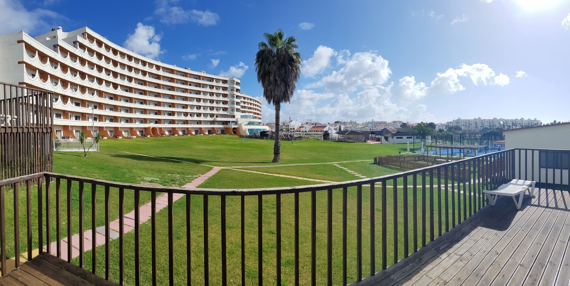 A hotel with a curved building, a grassy courtyard, and a palm tree.