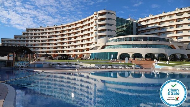 Et hotel med en stor swimmingpool, flere balkoner og et moderne arkitektonisk design.