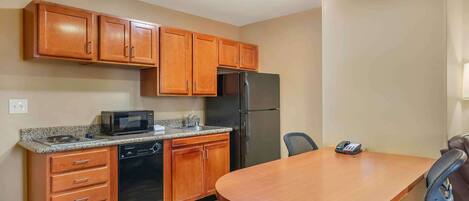 Una cocina compacta con armarios de madera, microondas, refrigerador, lavavajillas y una mesa de comedor con sillas.