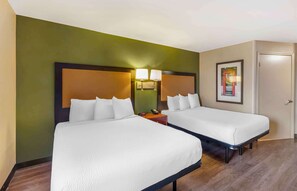 Een hotelkamer met twee bedden, een houten vloer, groene wanden en een ingelijst schilderij.