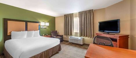 A hotel room with a large bed, a desk, a television, a chair, and a window with curtains.