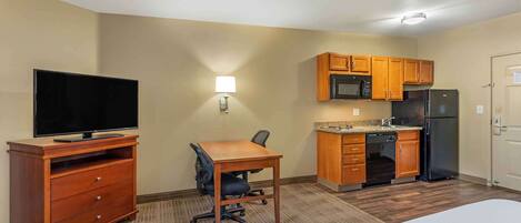 Habitación de hotel con televisión, escritorio con silla, kitchenette con microondas y refrigerador, y una puerta.