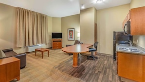 Hotelkamer met een eettafel, een bank, een televisie, een kitchenette en een groot raam met gordijnen.