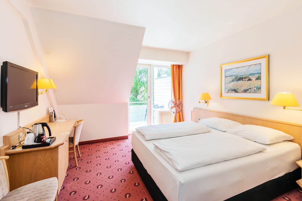 Une chambre d’hôtel comprenant un lit, un bureau avec une chaise, une télévision et deux lampes.