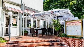 Ein Sitzbereich im Freien mit Tischen und Stühlen, der von Sonnenschirmen beschattet wird, und ein Schild für das Restaurant Spice of India Tandoori & Curry.