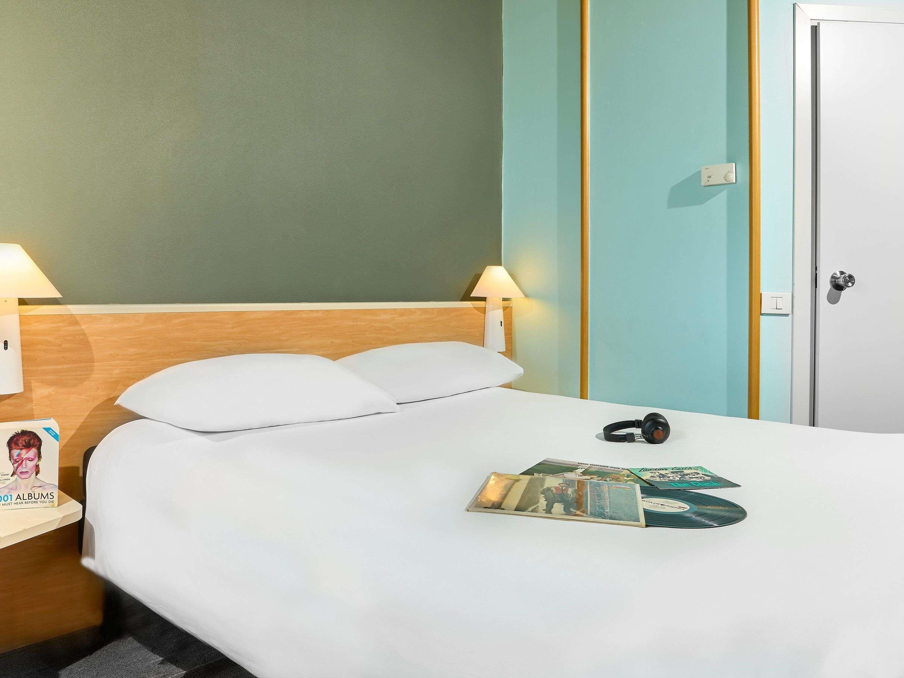 A hotel room with a bed, two bedside lamps, a door, and a magazine on the bed.
