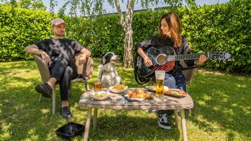 Two people sitting on wicker chairs outdoors with a dog, a guitar, and food on a table.