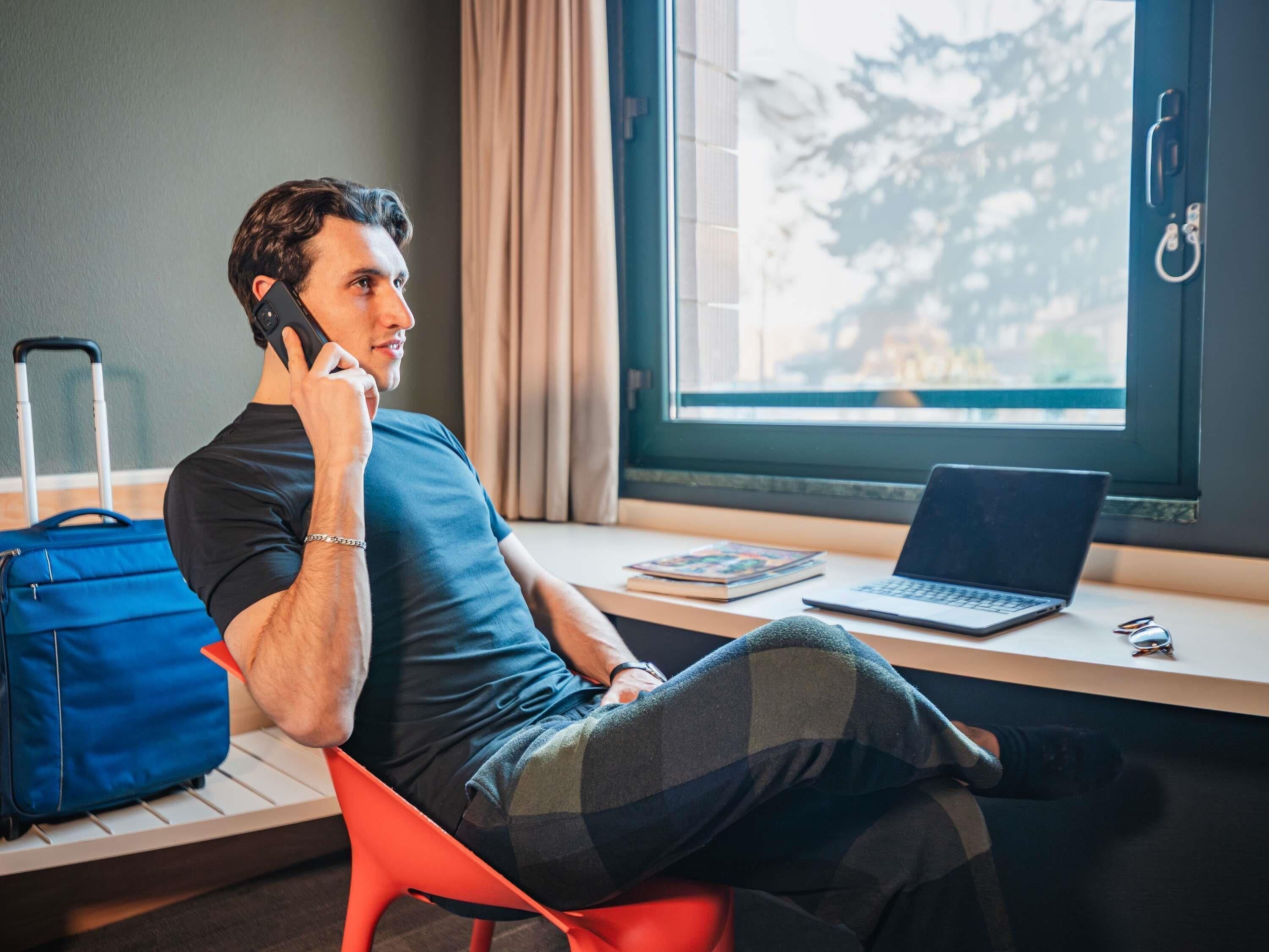 A person sitting at a desk with a laptop, a blue suitcase, and a book.