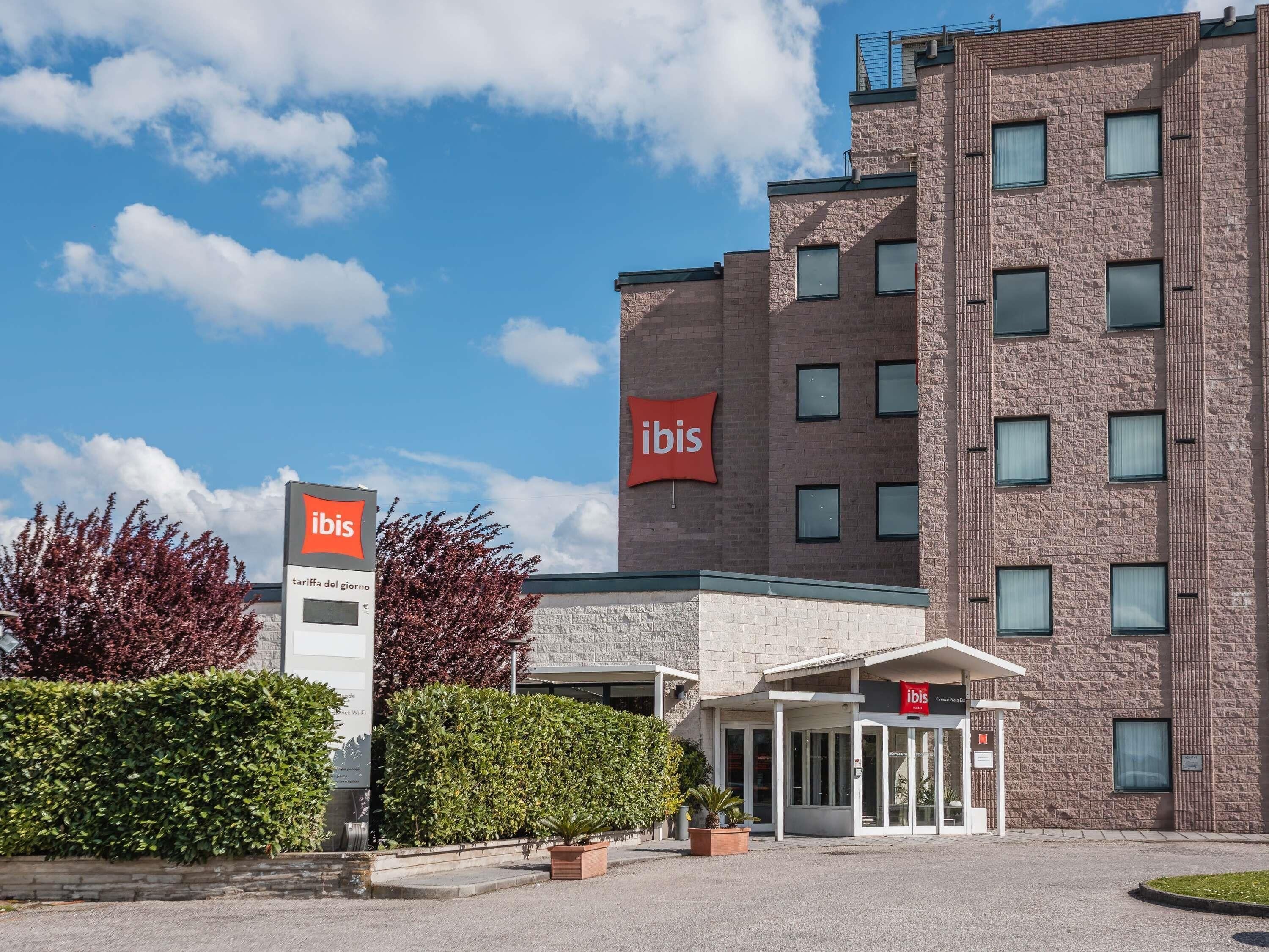A modern hotel with a prominent 'ibis' sign, a brick facade, and a covered entrance.